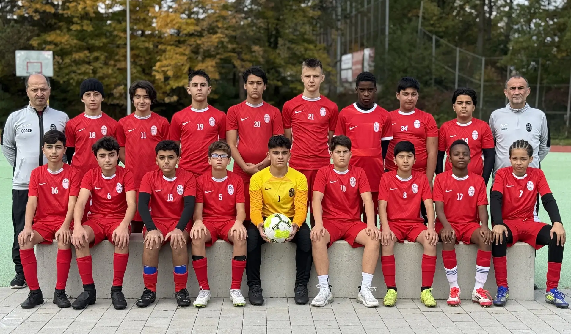 Gruppenfoto der C2-Junioren Fußballmannschaft in roten Trikots mit Torwart in Gelb vor herbstlicher Kulisse.