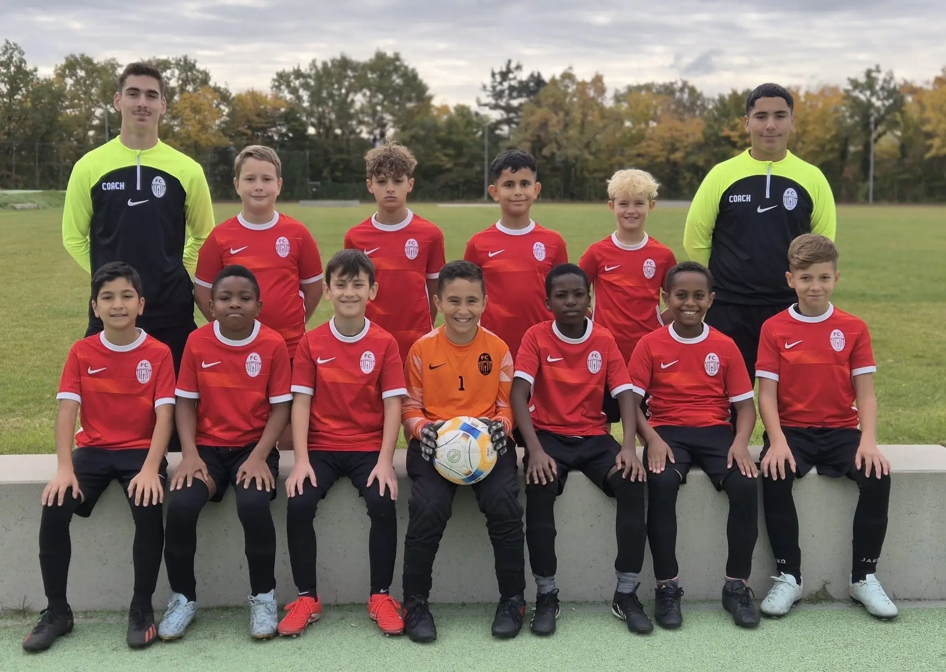 Gruppenfoto der E1-Junioren Fußballmannschaft in roten Trikots mit Torwart und Trainern auf einem Sportplatz.