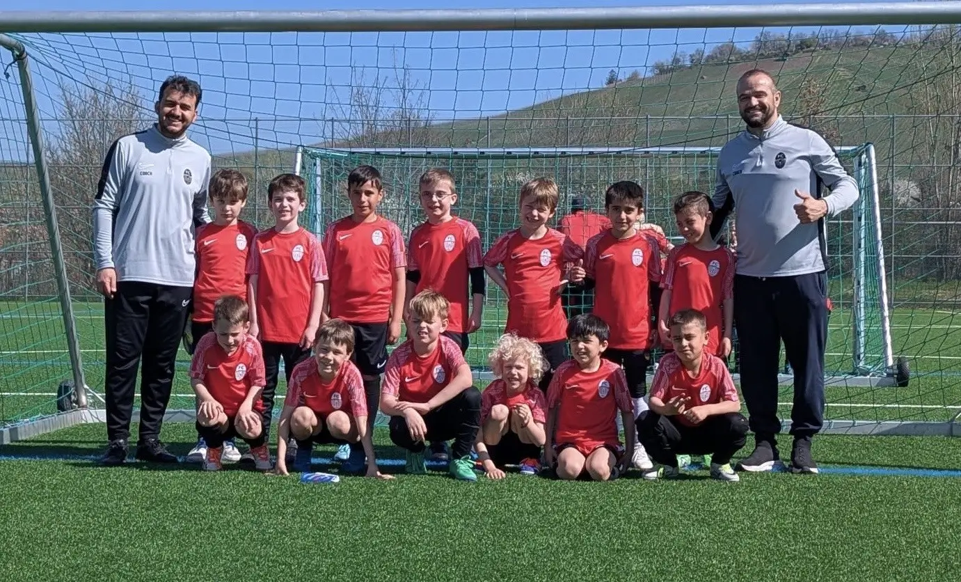 Gruppenfoto der F2-Junioren Fußballmannschaft (U8) in roten Trikots mit Trainern vor einem Großfeldtor auf Kunstrasen.